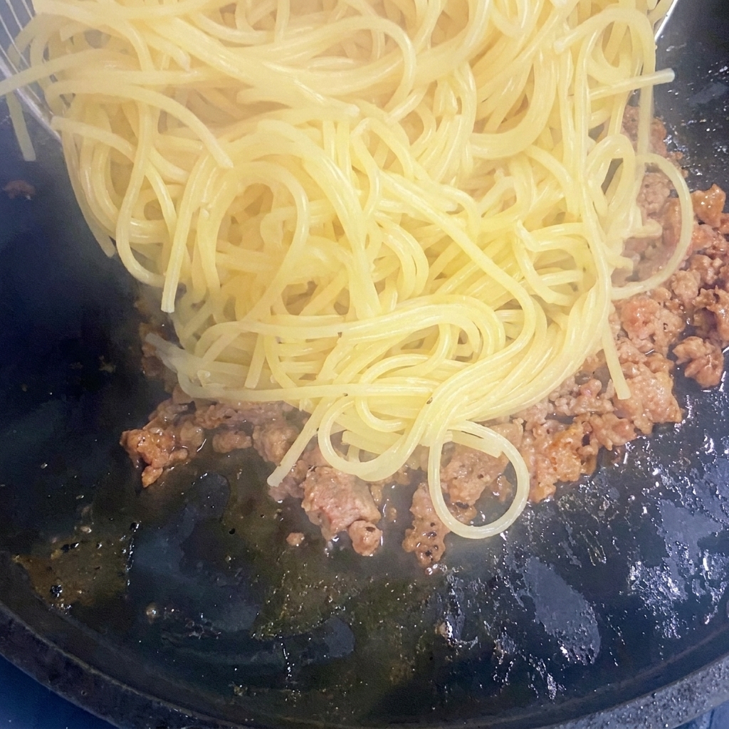Gekochte Spaghetti werden in eine Pfanne mit gebräuntem Hackfleisch gegeben.