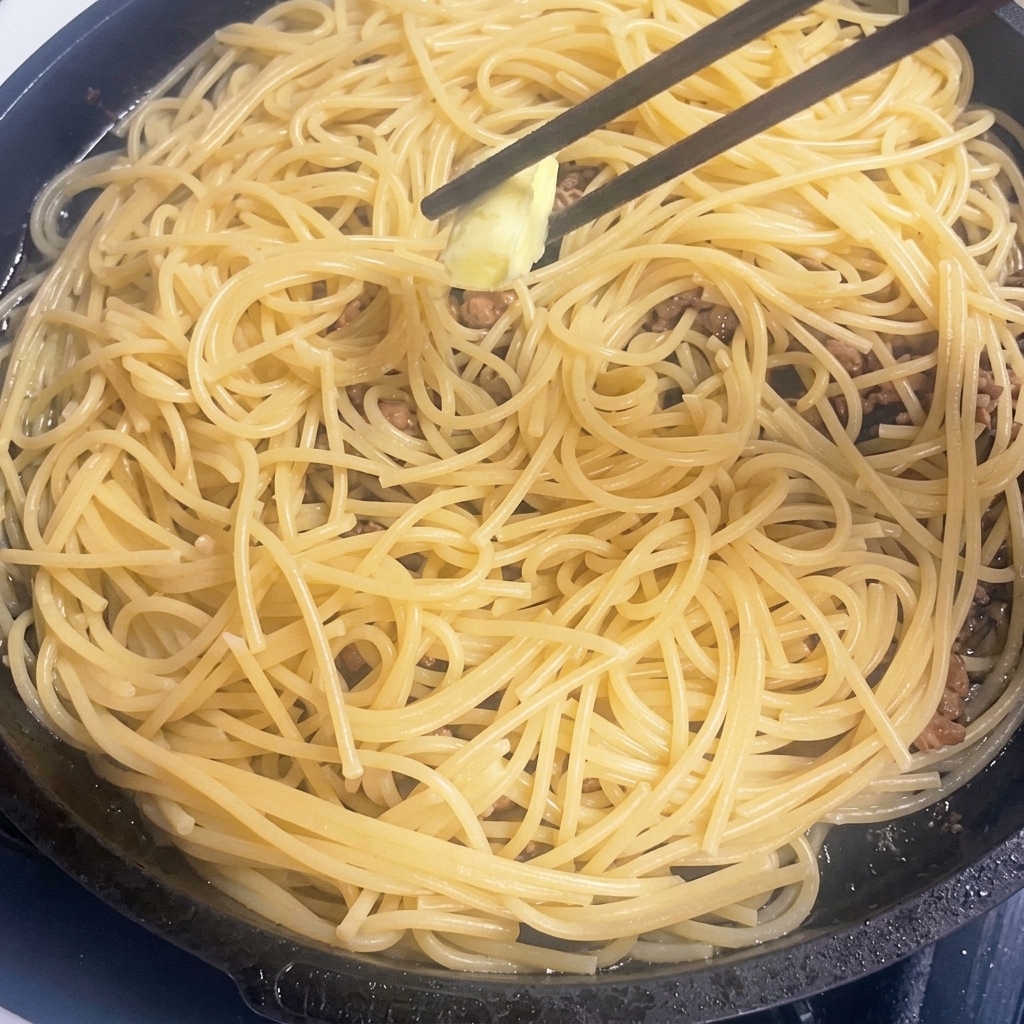 Ein kleines Stück Butter schmilzt in einer Pfanne mit heißer Pasta und Fleisch.