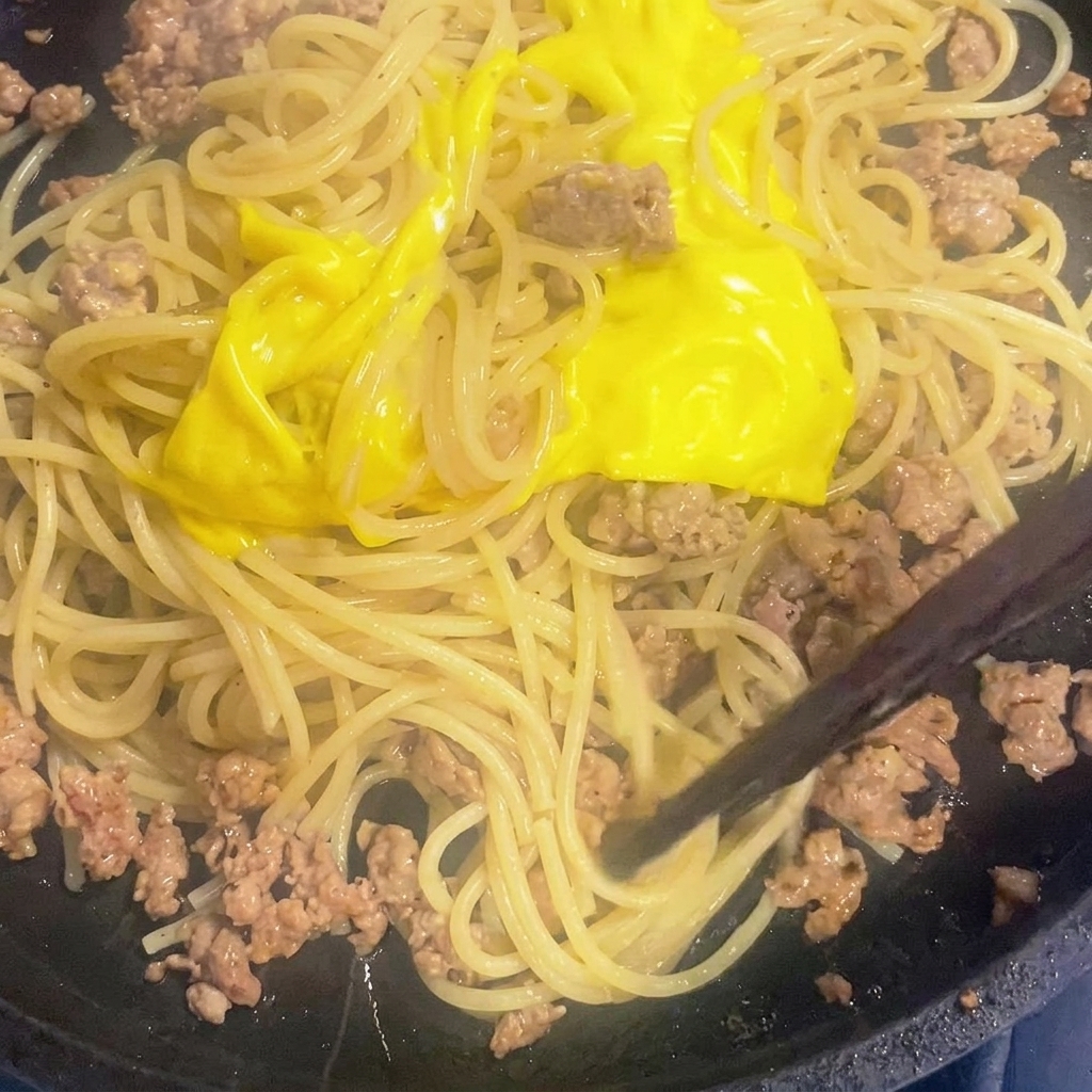 Geschmolzener Käse wird in einer Pfanne unter die Spaghetti-Fleisch-Mischung gerührt.