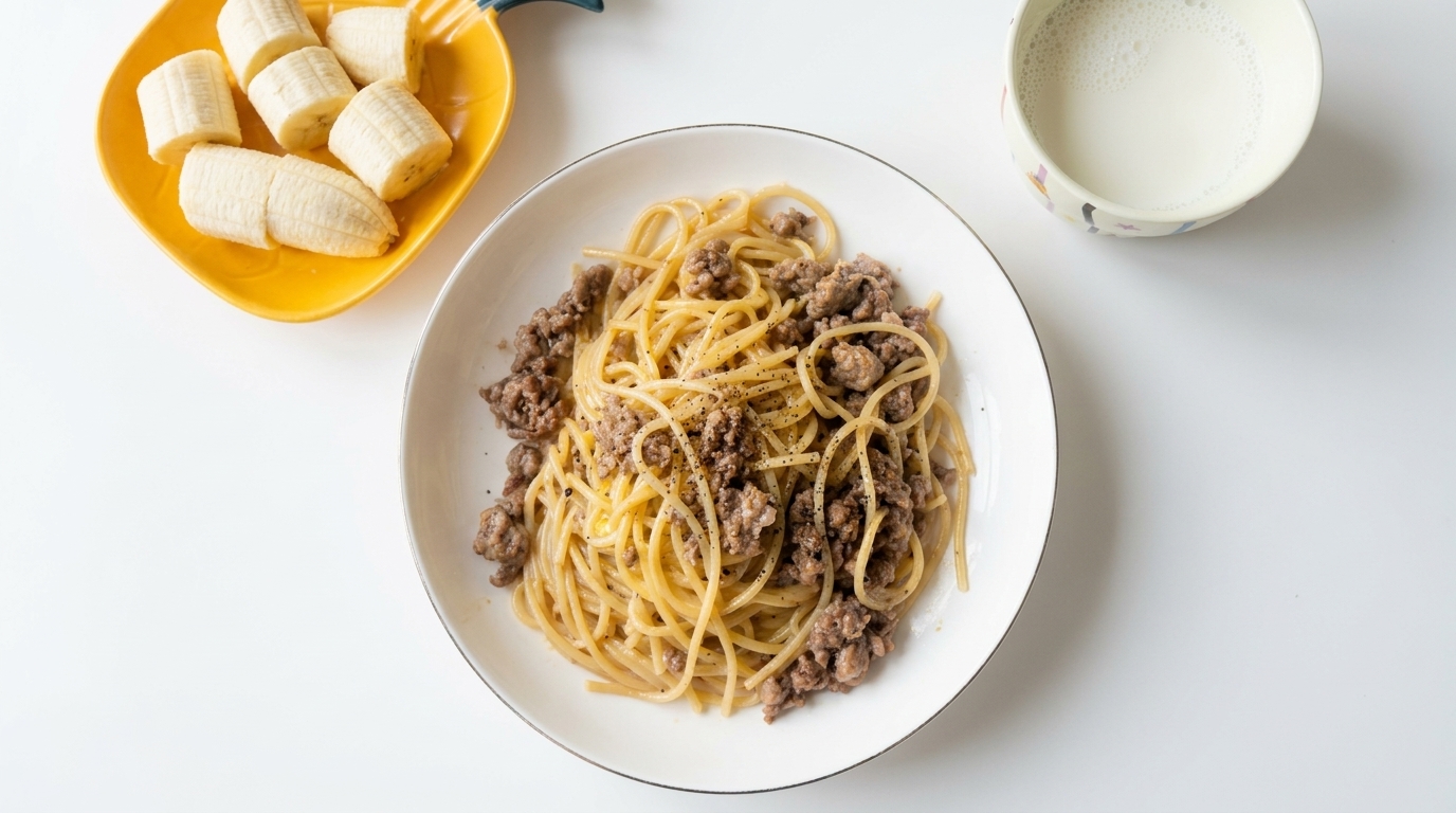 Ein Teller cremige Pfeffer-Pasta mit Hackfleisch, serviert mit frischen Bananenscheiben und einem Glas Milch.