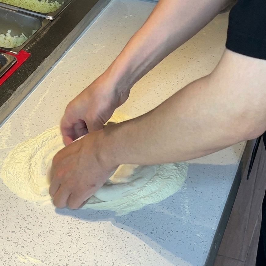 Hände drücken und dehnen Pizzateig in einem Mehlhaufen auf einer weißen Oberfläche.