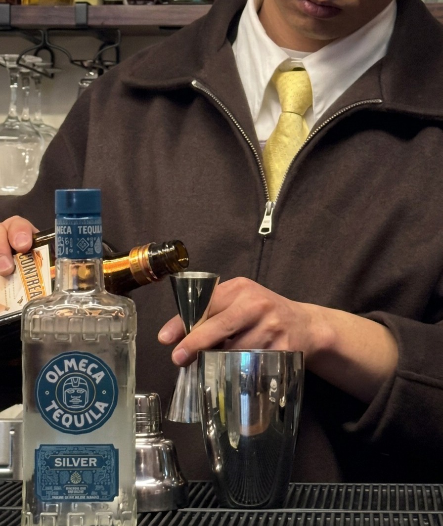 Triple Sec, der aus einer Flasche in einen Jigger über einem Shaker gegossen wird.
