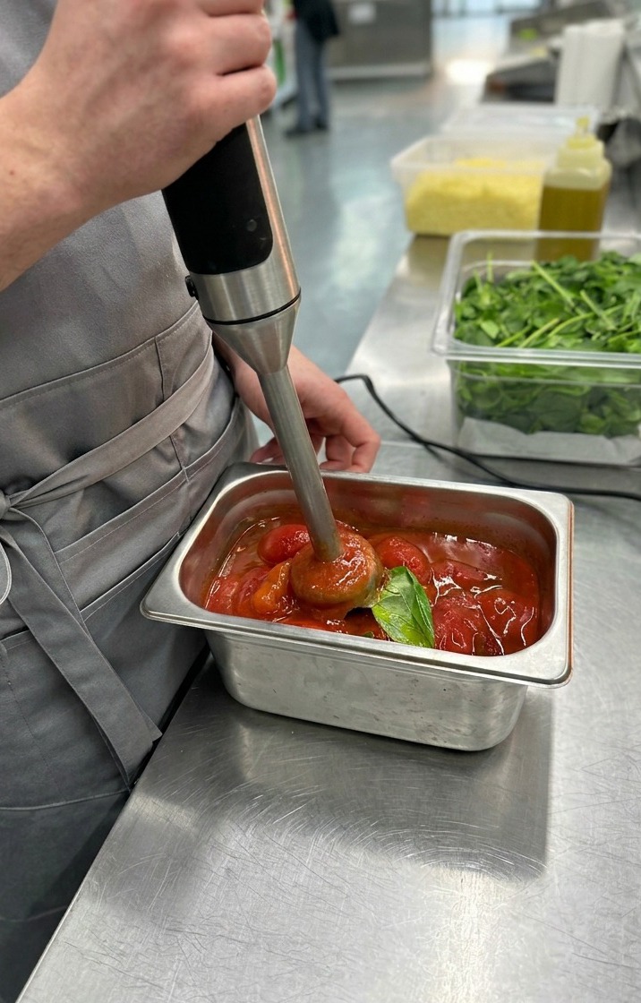 Ein Stabmixer verarbeitet geschälte Tomaten und Basilikum zu einer glatten, leuchtend roten Pizzasauce.