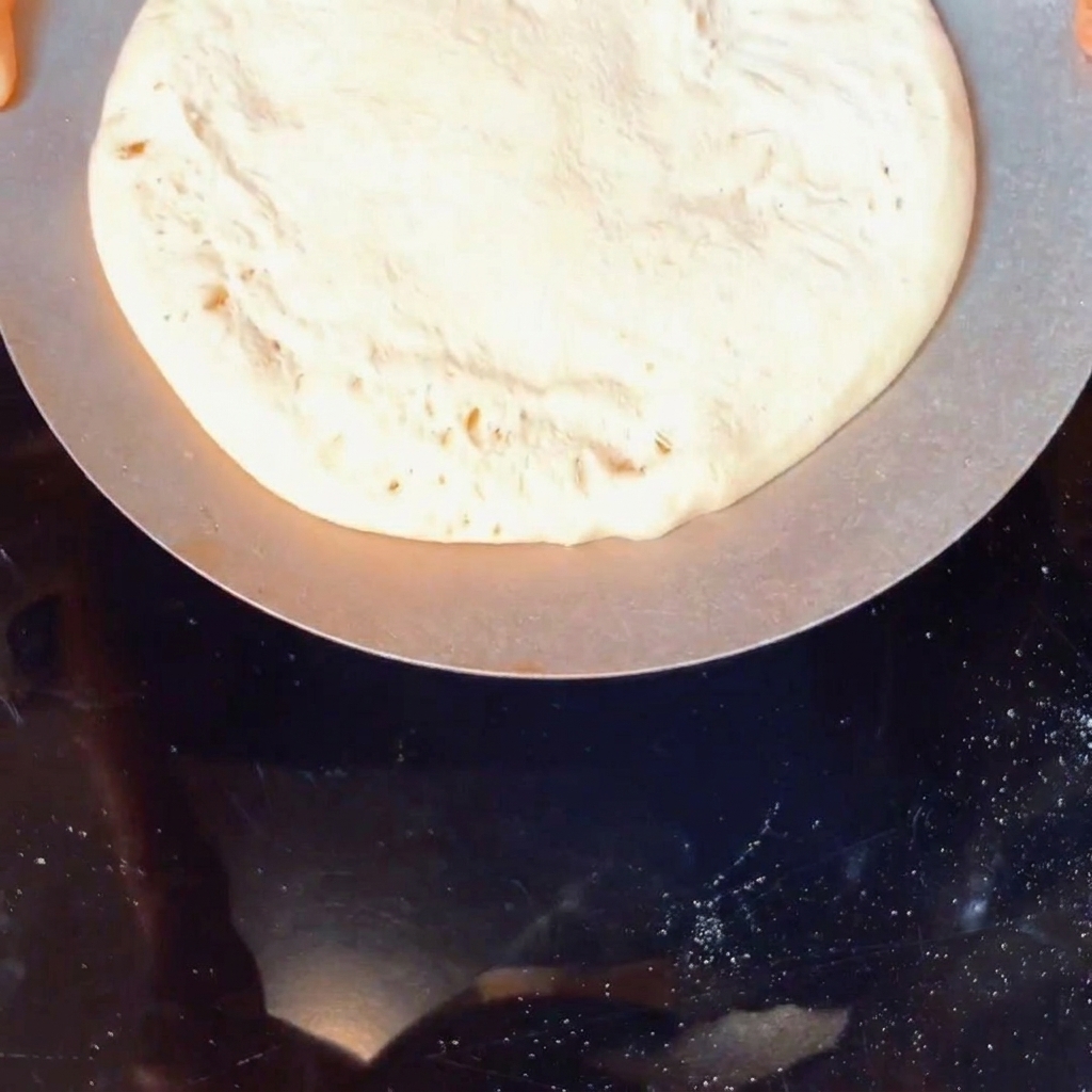 Eine Kugel roher Pizzateig, die in einem Behälter mit gelbem Maismehl gewendet wird.