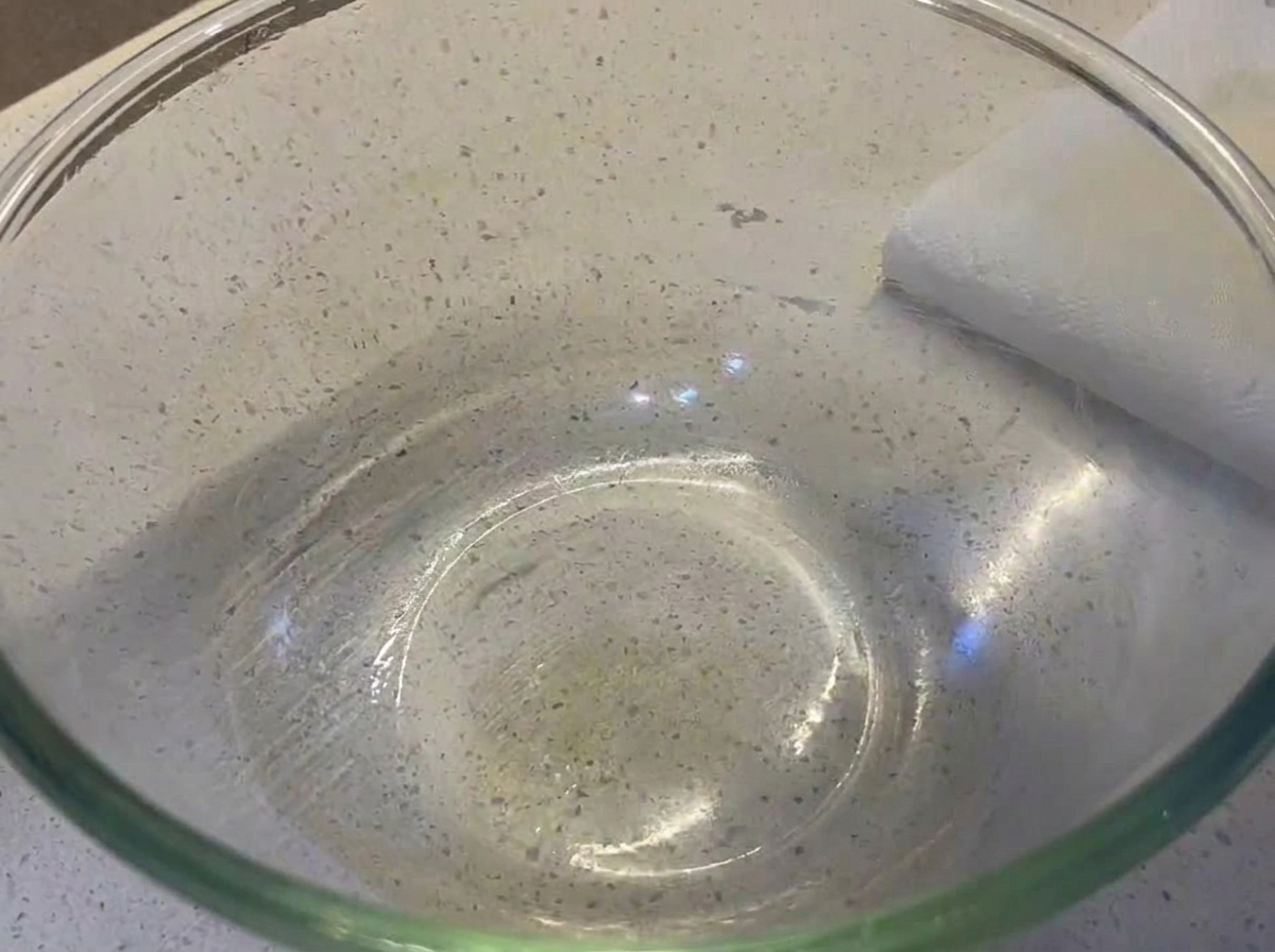 Eine glatte, runde Pizzateigkugel ruht in einer großen, klaren und leicht geölten Glasschüssel.