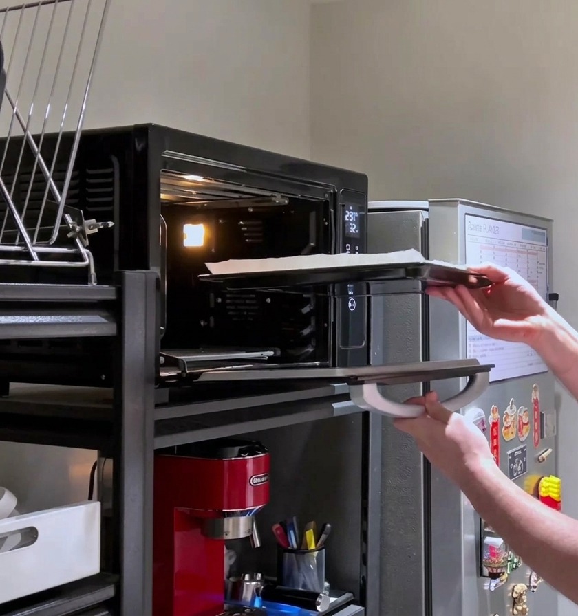 Eine Person schiebt eine mit Käse belegte rechteckige Pizza für den letzten Backvorgang zurück in den heißen Ofen.