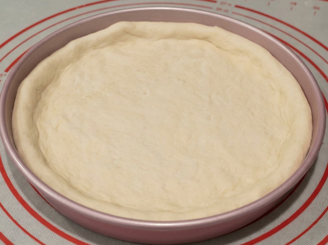 Teig in einer 23-cm-Pizzapfanne, wobei die Ränder von Hand geformt werden.
