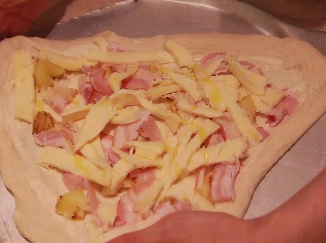 Die Ränder des Pizzateigs werden nach innen gefaltet, um den Belag zu umschließen.