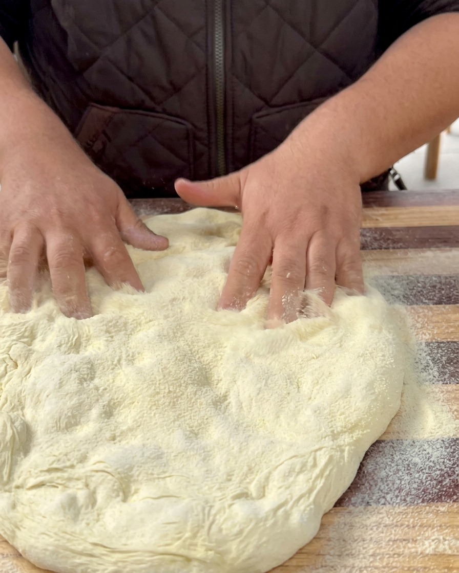 Ausgerollter Pizzateig auf einem mit Backpapier ausgelegten Backblech.