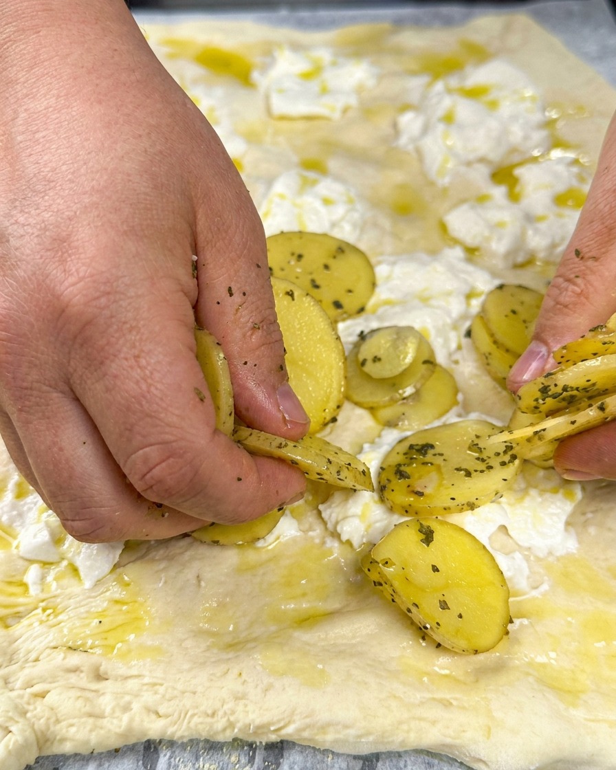 Kartoffelscheiben auf der Käsebasis, bestreut mit frischen Kräutern.