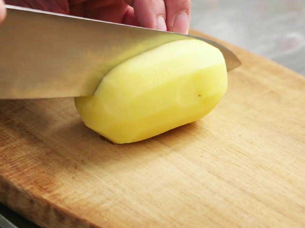 Rohe Kartoffelstücke auf einem Holzschneidebrett.