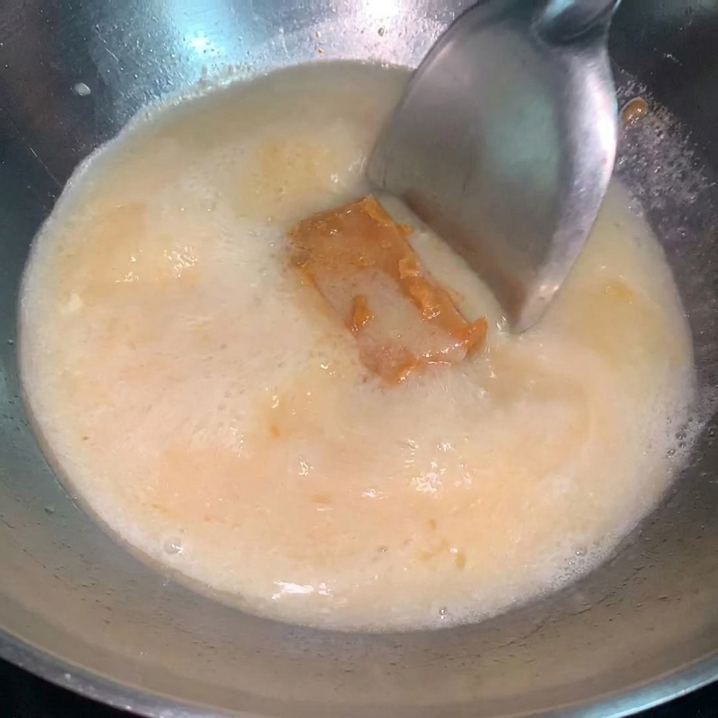 Ein Löffel konzentrierte Miso-Sauce wird in einen Topf mit köchelnder Ramen-Brühe gerührt.