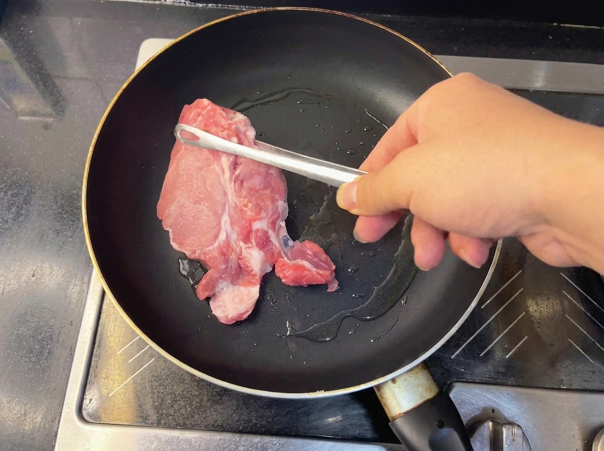 Zwei Stücke roher Schweinenacken braten in einer heißen Pfanne.