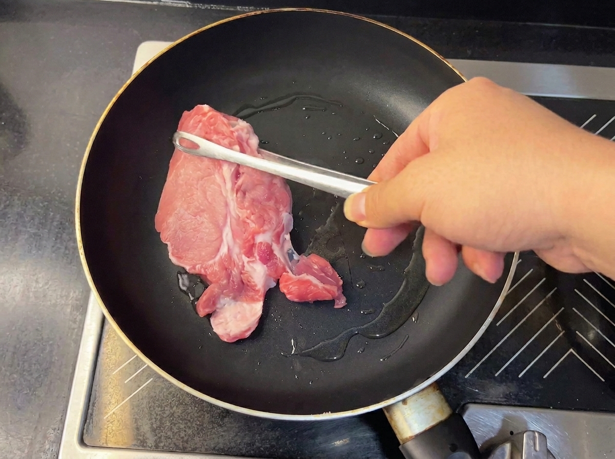 Zart gebräunte Fleischstücke werden mit einer Küchenzange aus der Pfanne gehoben.