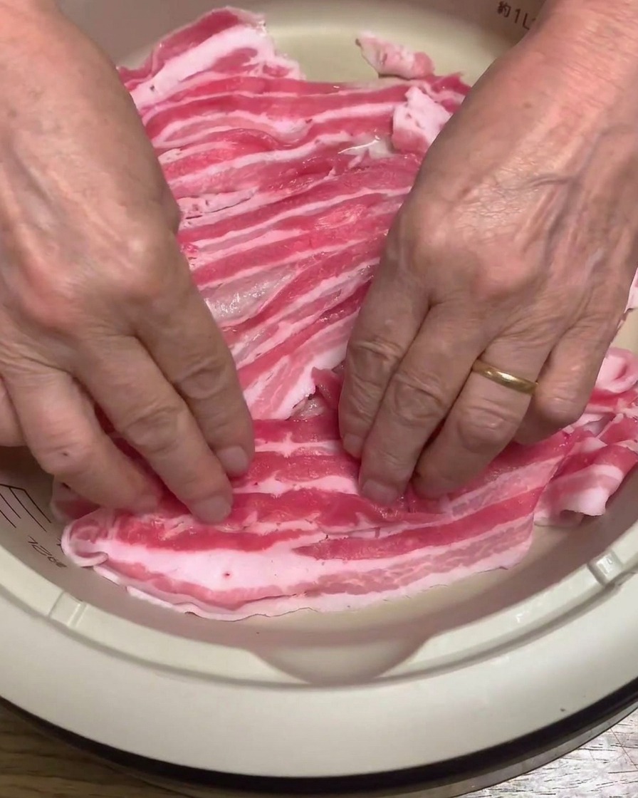 Nahaufnahme von rohen Schweinebauchscheiben, die säuberlich auf dem Boden eines elektrischen Topfes angeordnet werden.