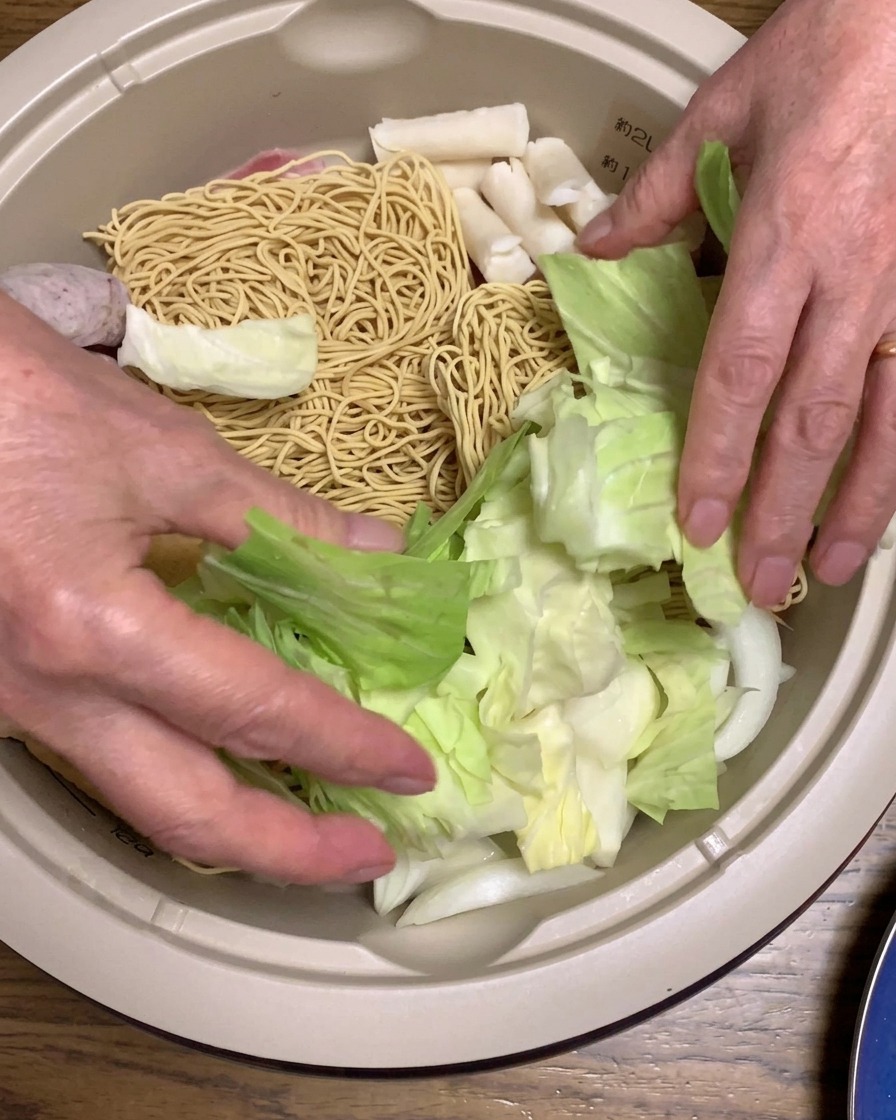 Gehackter Kohl und leuchtend rote Surimi-Stäbchen werden in den Topf gelegt.