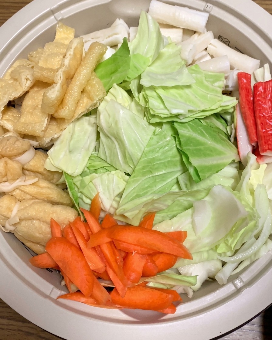 Heißes Wasser wird in den Topf gegossen, der mit rohen Ramen-Zutaten wie Kohl, Karotten und Tofu gefüllt ist.