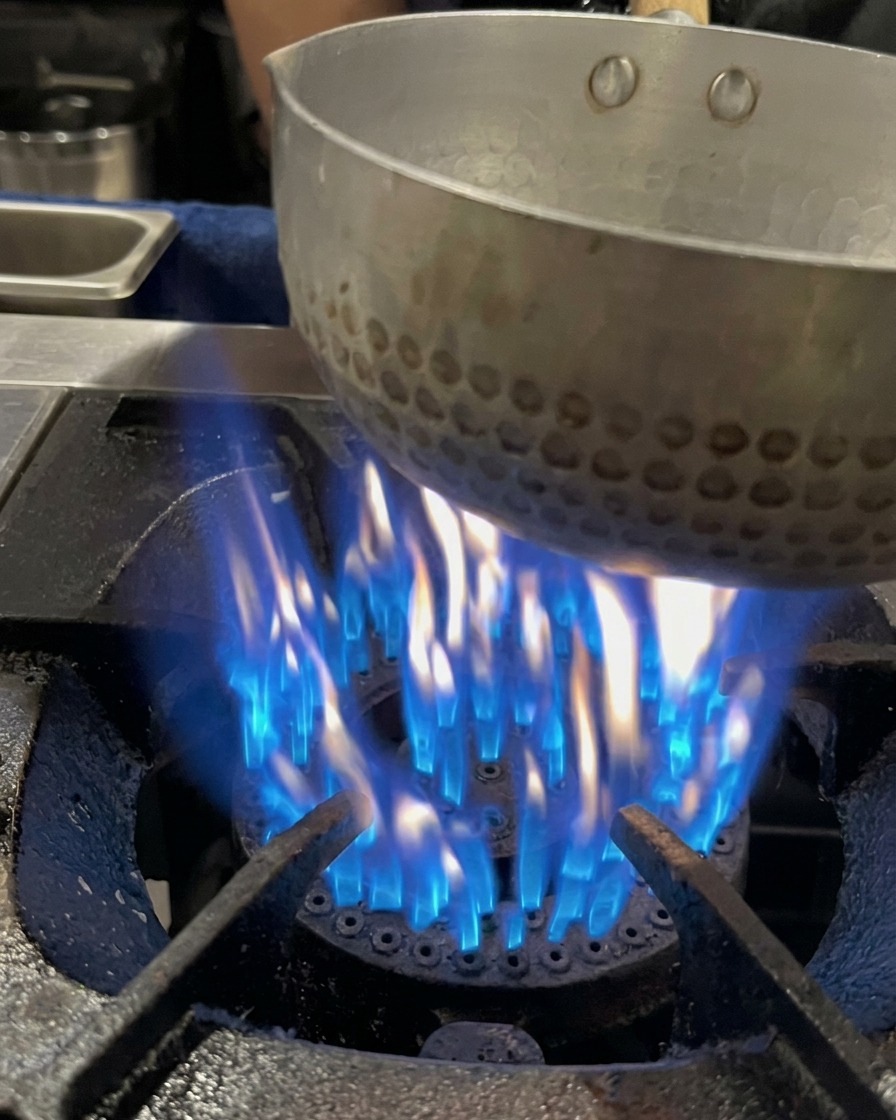 Schweineknochenbrühe wird in einen Topf über einer blauen Gasflamme gegossen.