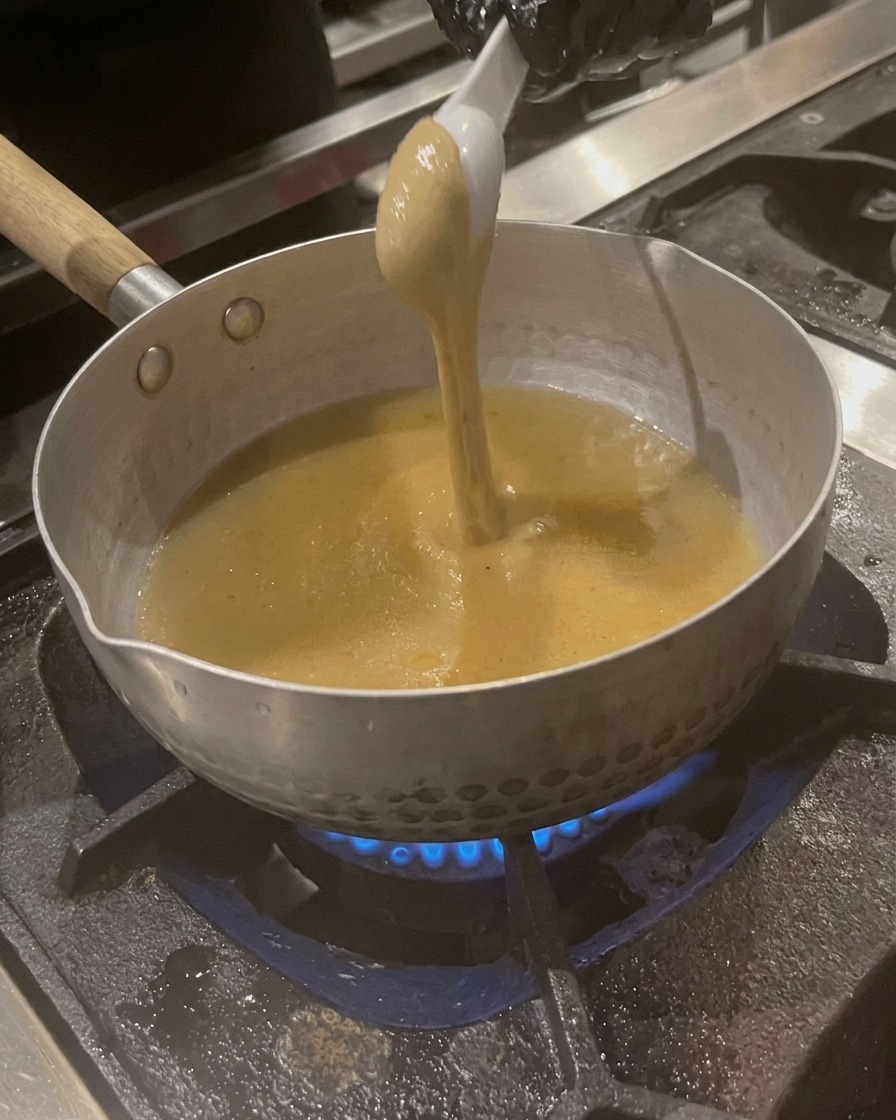 Ein Löffel dicke Sesampaste wird in die köchelnde Brühe eingerührt.