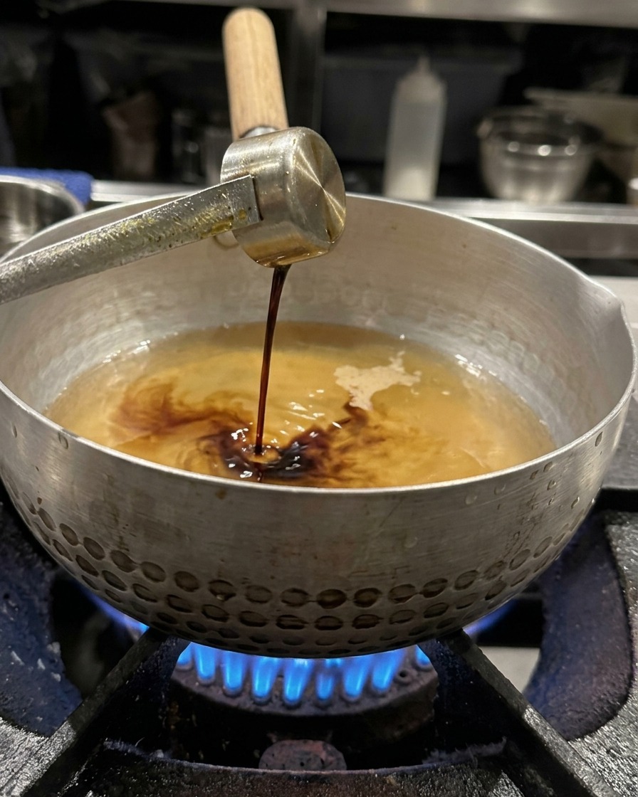 Sojasauce wird aus einer Schöpfkelle in die Brühe gegeben.