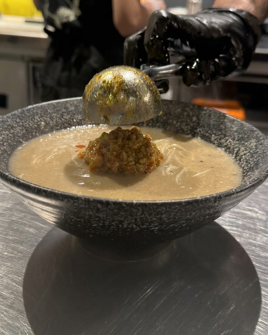 Rotes Chili-Öl wird in kreisförmigen Mustern über die Suppe geträufelt.