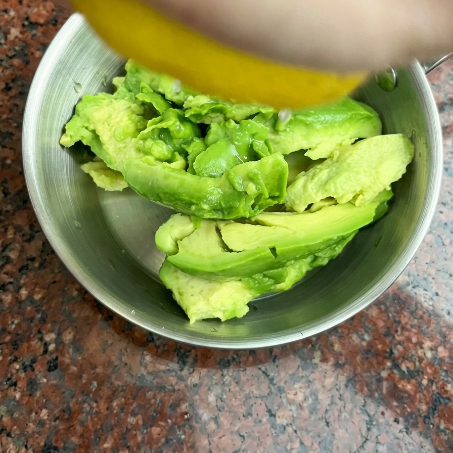 Frischer Zitronensaft wird von Hand auf halbierte Avocados in einer kleinen Edelstahlschüssel gepresst.