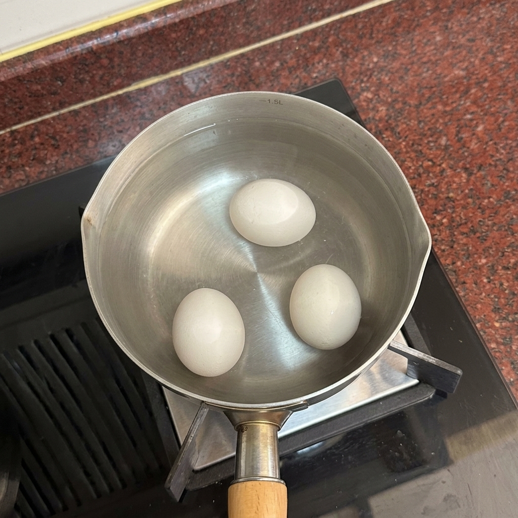 Drei weiße Eier liegen am Boden eines Topfes, der mit klarem, heißem Wasser gefüllt ist.
