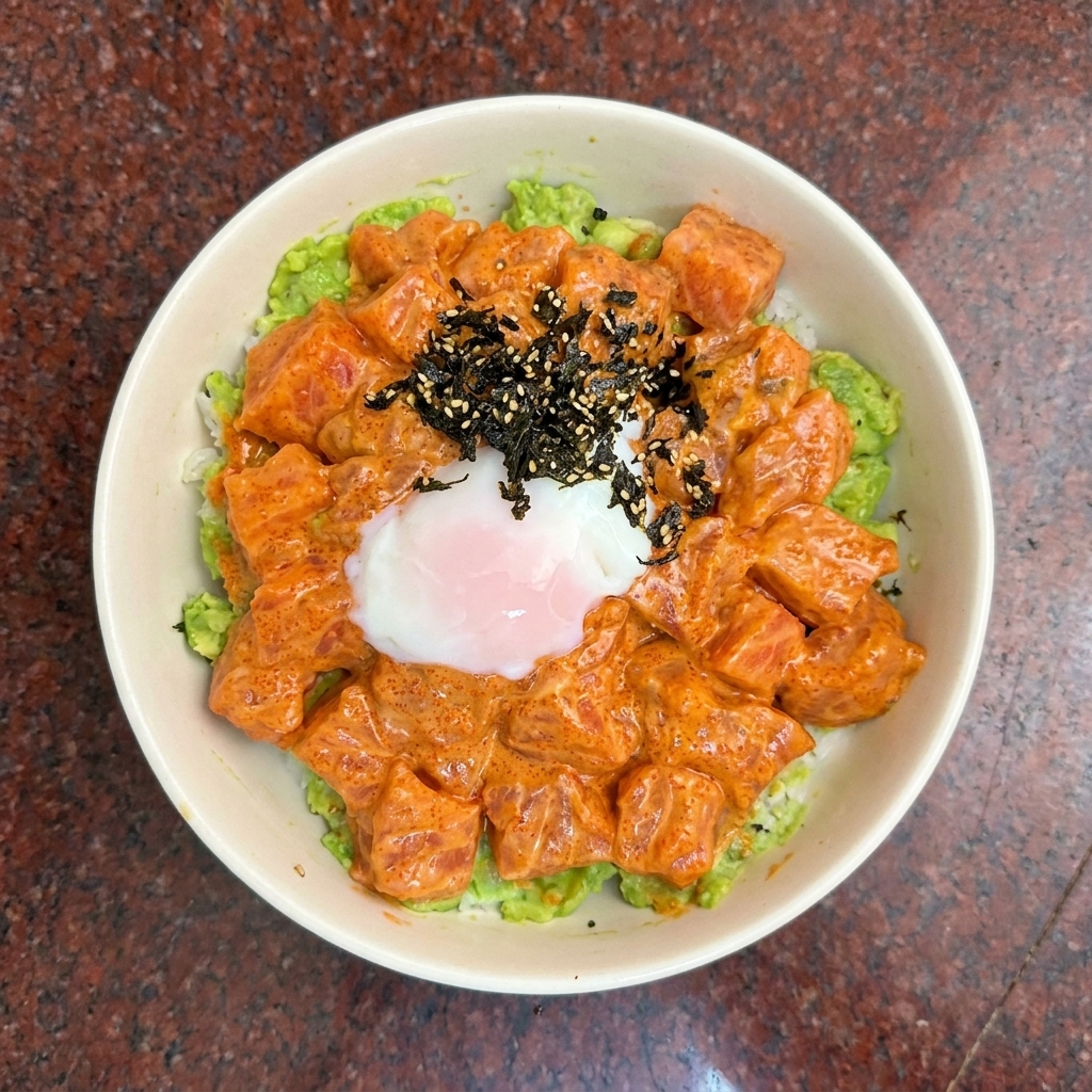 Eine Draufsicht auf eine Lachs-Poke-Bowl, garniert mit einem weichgekochten Ei und dunklem Algen-Gewürz.