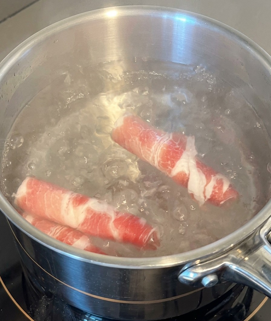 Zwei dünne Scheiben rohes Rindfleisch werden in einen Edelstahltopf mit kochendem Wasser getaucht.