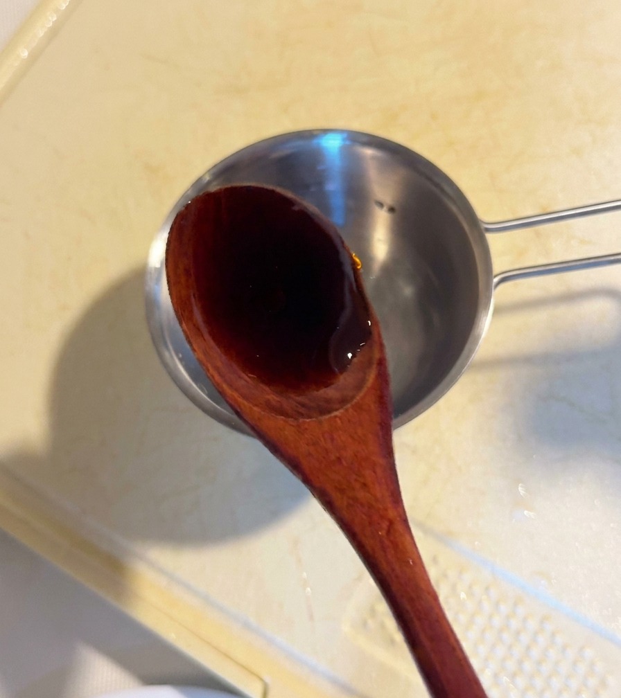 Ein Holzlöffel gießt dunkle Austernsauce in eine kleine Metallschüssel zu den anderen Saucenzutaten.