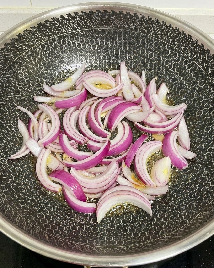 Rote Zwiebelstreifen werden in einem heißen Wok mit Wabenmuster in glänzendem Öl angebraten.