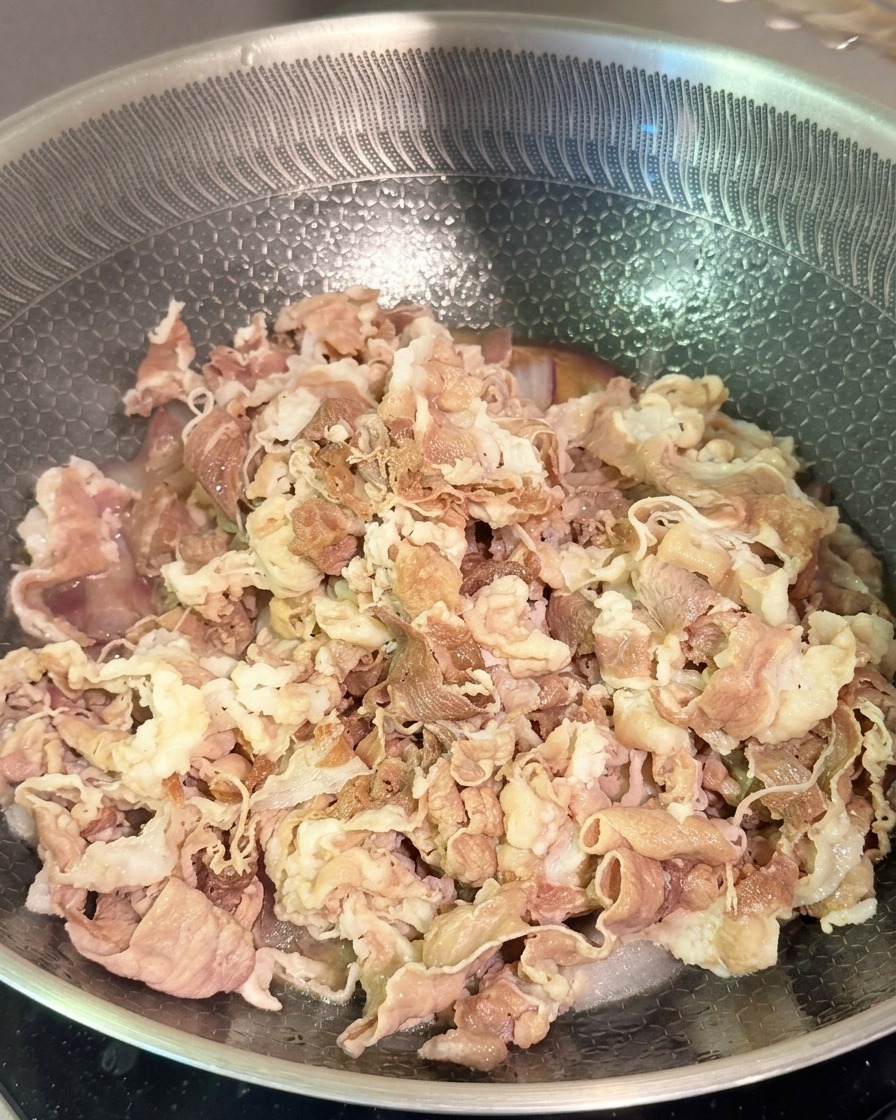Zarte blanchierte Rindfleischstreifen werden mit roten Zwiebeln und dunkler Sauce in einem Edelstahl-Wok vermengt.