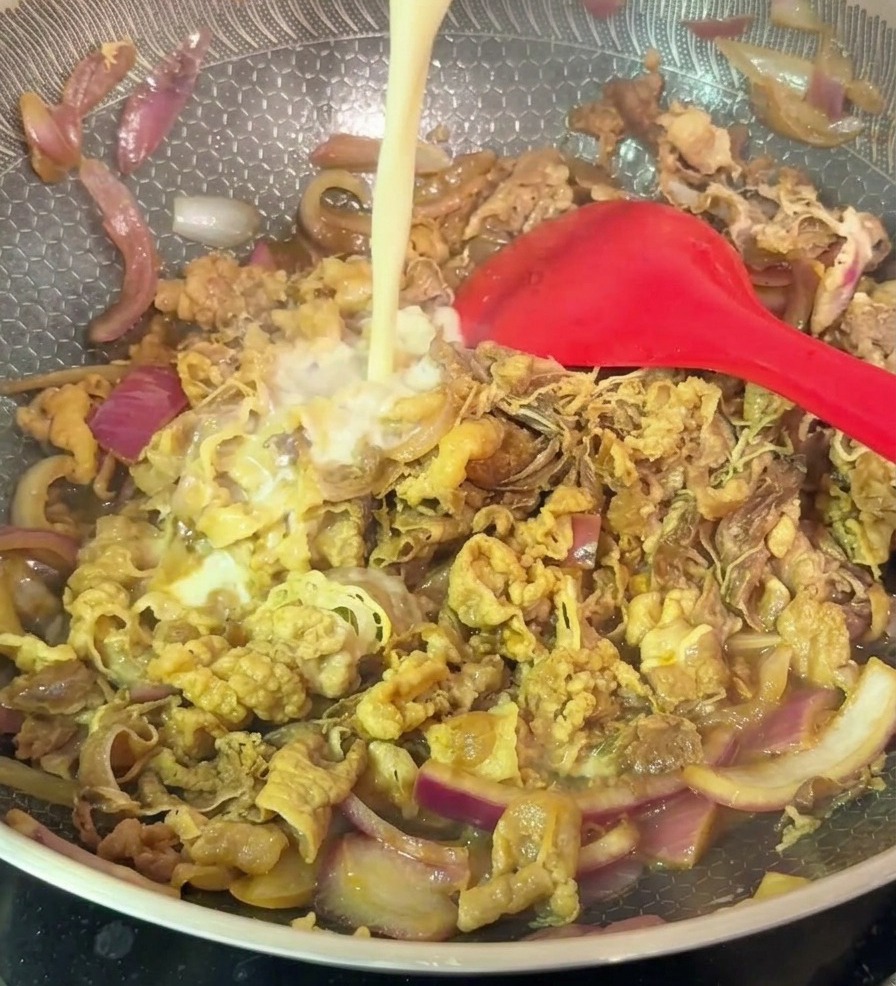 Die angerührte Speisestärke wird in einen Wok mit Rindfleisch und roten Zwiebeln gegossen.