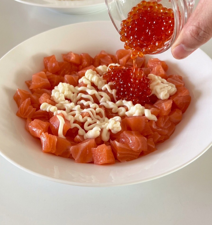 Frisch gewürfelter Lachs in einer weißen Schüssel wird mit leuchtend rotem Fischrogen und cremiger Mayonnaise bedeckt.