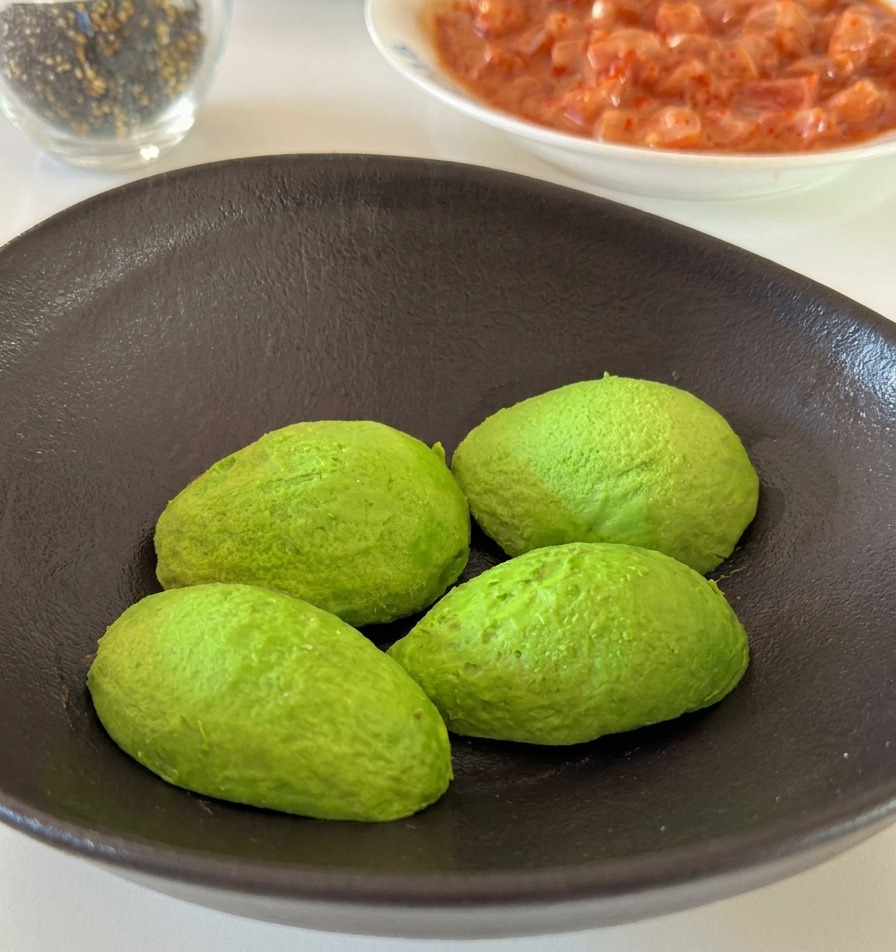Eine Hand drückt eine frische Zitronenspalte über grüne Avocadohälften in einer Keramikschale aus.