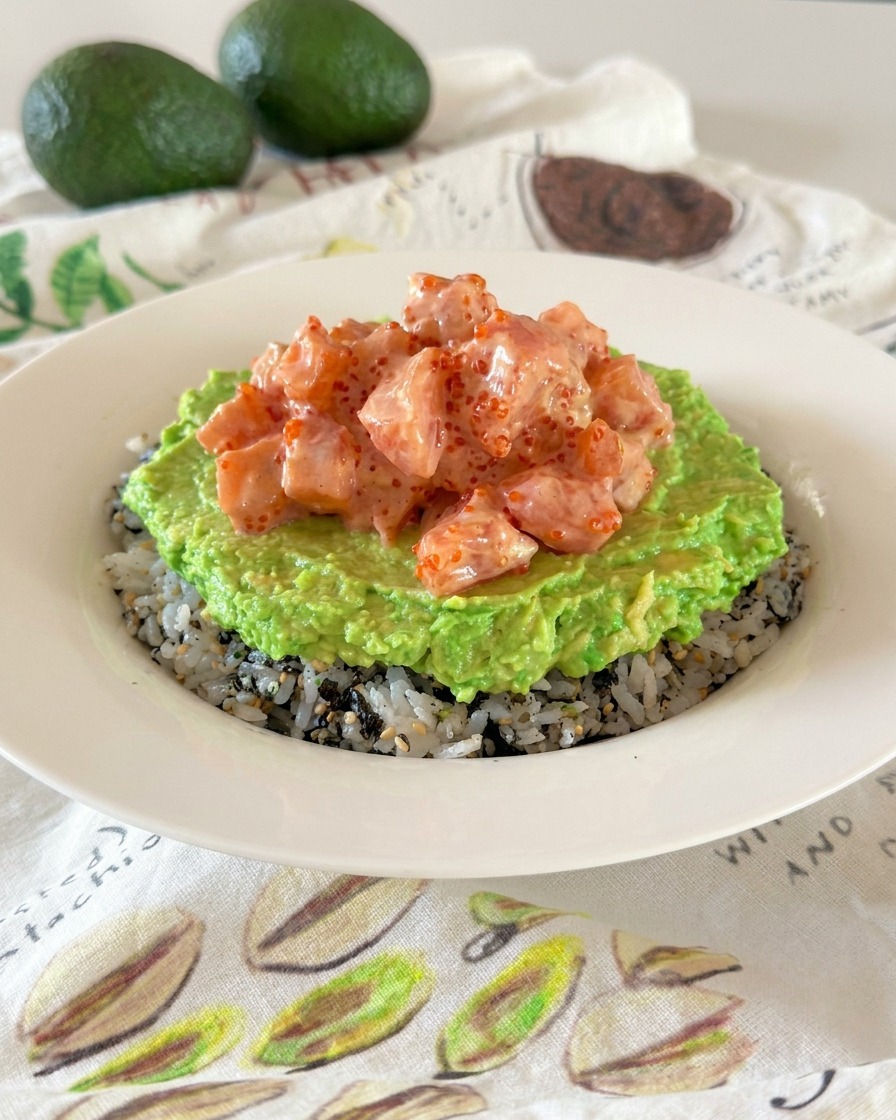 Eine Poke Bowl mit deutlich erkennbaren Schichten aus gewürztem Reis, zerdrückter Avocado und cremigen marinierten Lachswürfeln.