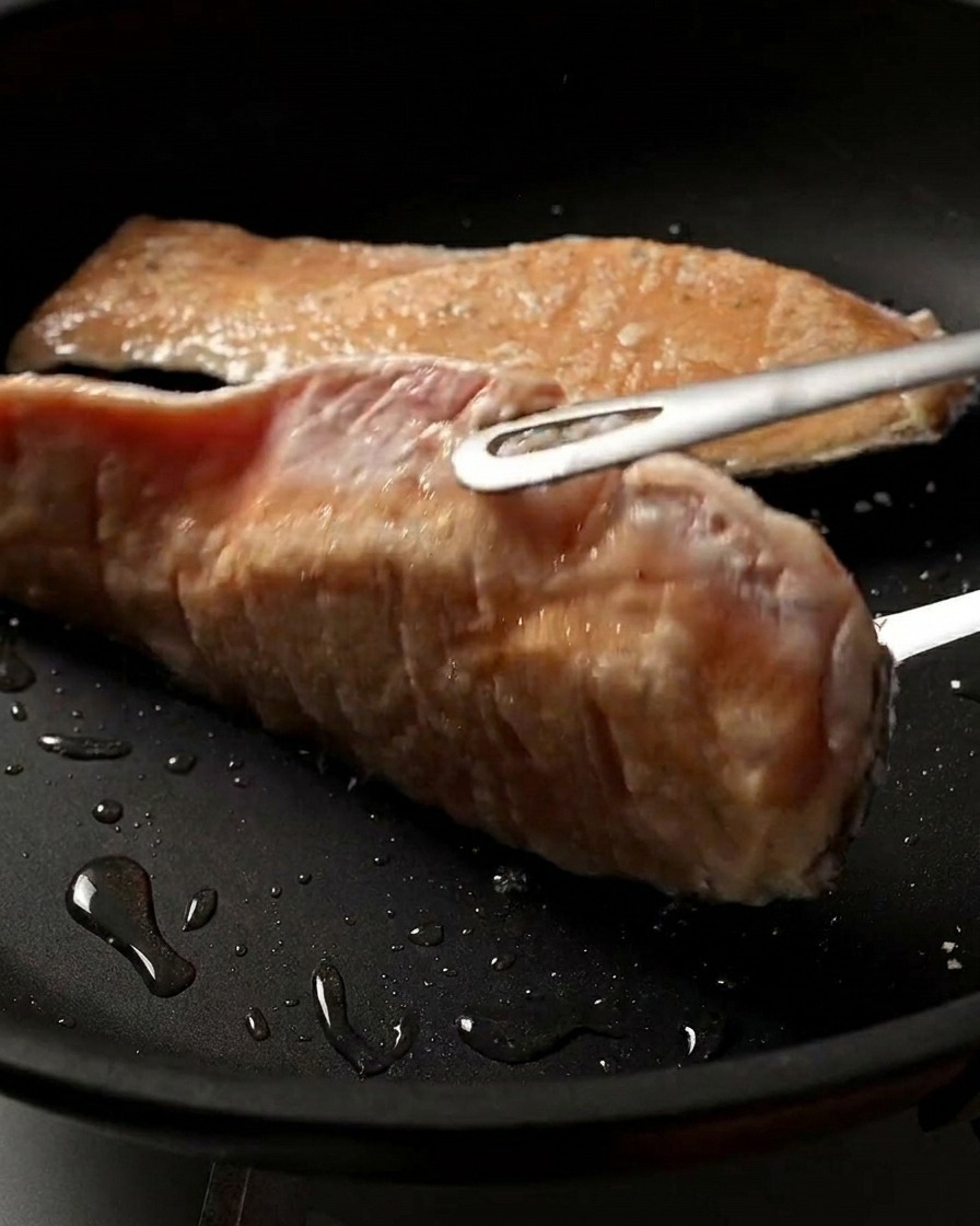 Nahaufnahme eines Lachsfilets, das in der Pfanne gewendet wird und eine perfekt gebräunte und knusprige Oberfläche zeigt.