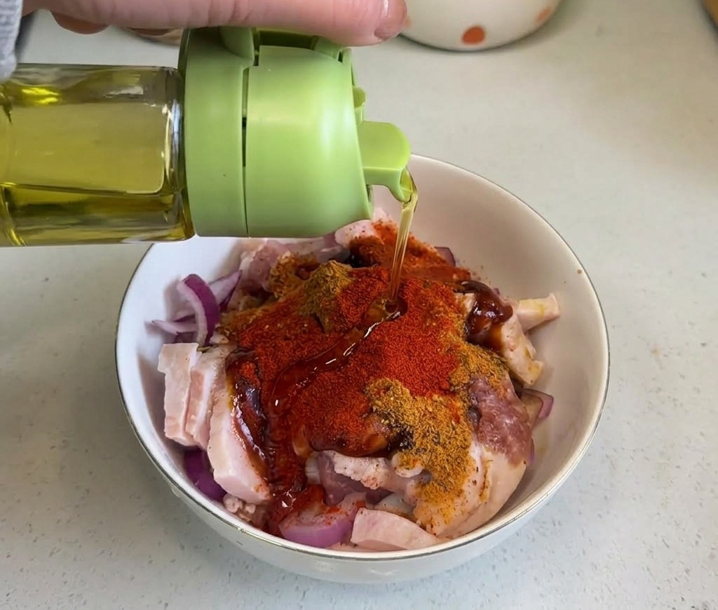 Klares Speiseöl wird aus einer grünen Flasche auf die gewürzte Schweinebauchmischung gegossen.