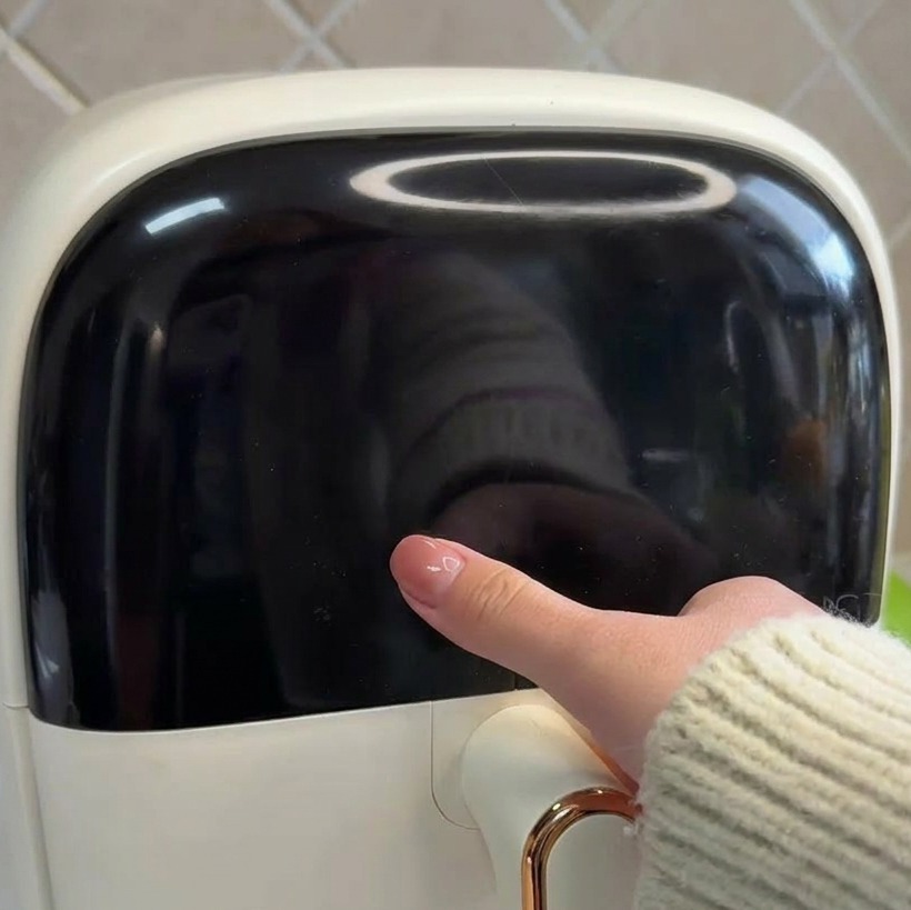 Nahaufnahme einer Hand, die das elegante schwarze digitale Bedienfeld einer weißen Heißluftfritteuse berührt.