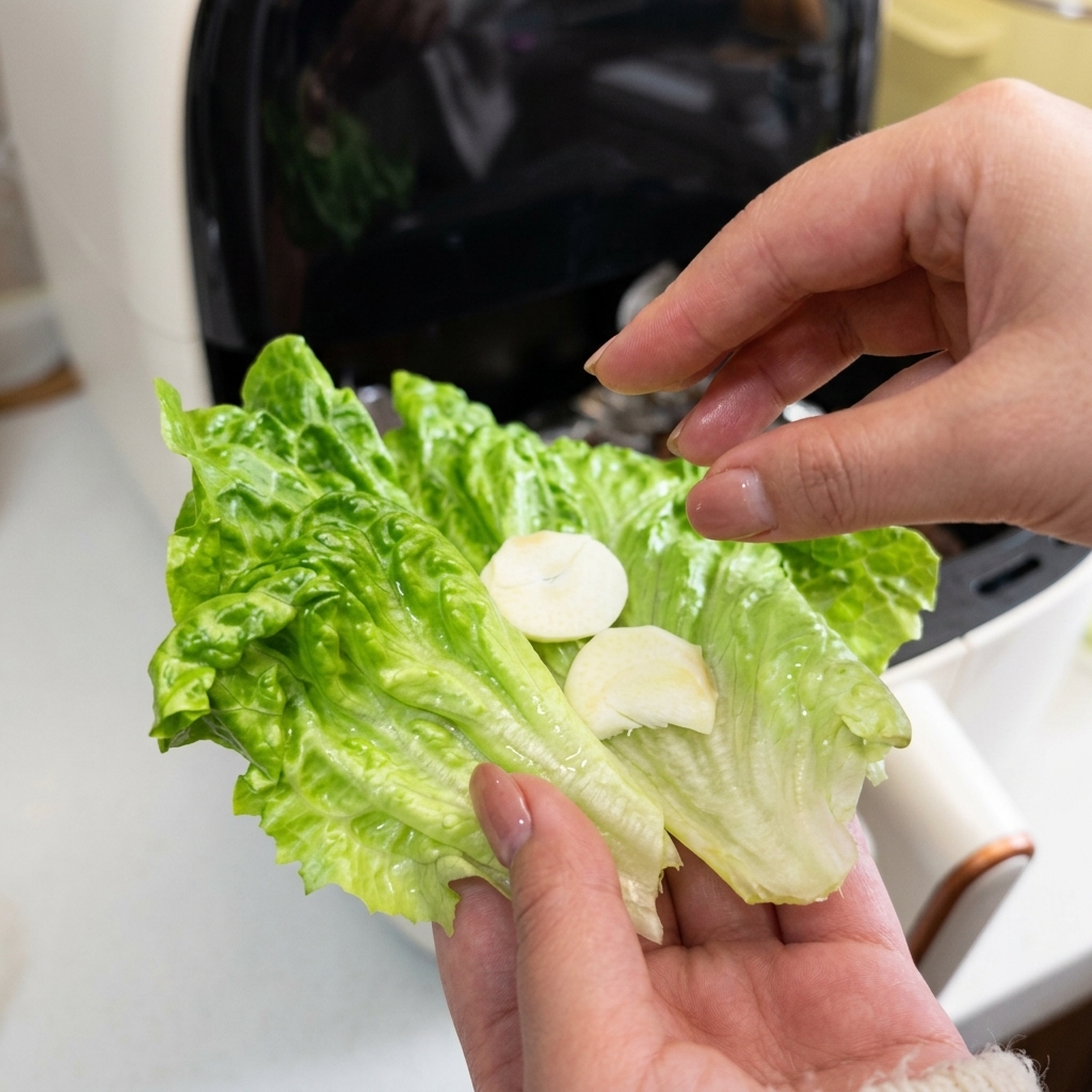 Nahaufnahme einer Hand, die ein grünes Salatblatt hält, das mit zwei Scheiben frischem weißem Knoblauch belegt ist.