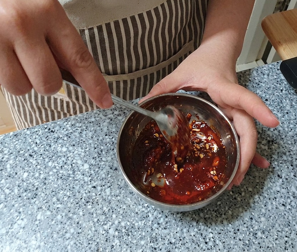 Eine tiefrote, dicke Marinade wird mit einem Edelstahllöffel in einer Metallschüssel glatt gerührt.