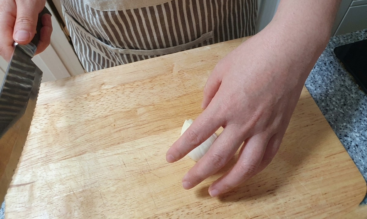 Dünne, vertikale Scheiben einer weißen Zwiebel werden mit einem Messer auf einer Holzoberfläche geschnitten.