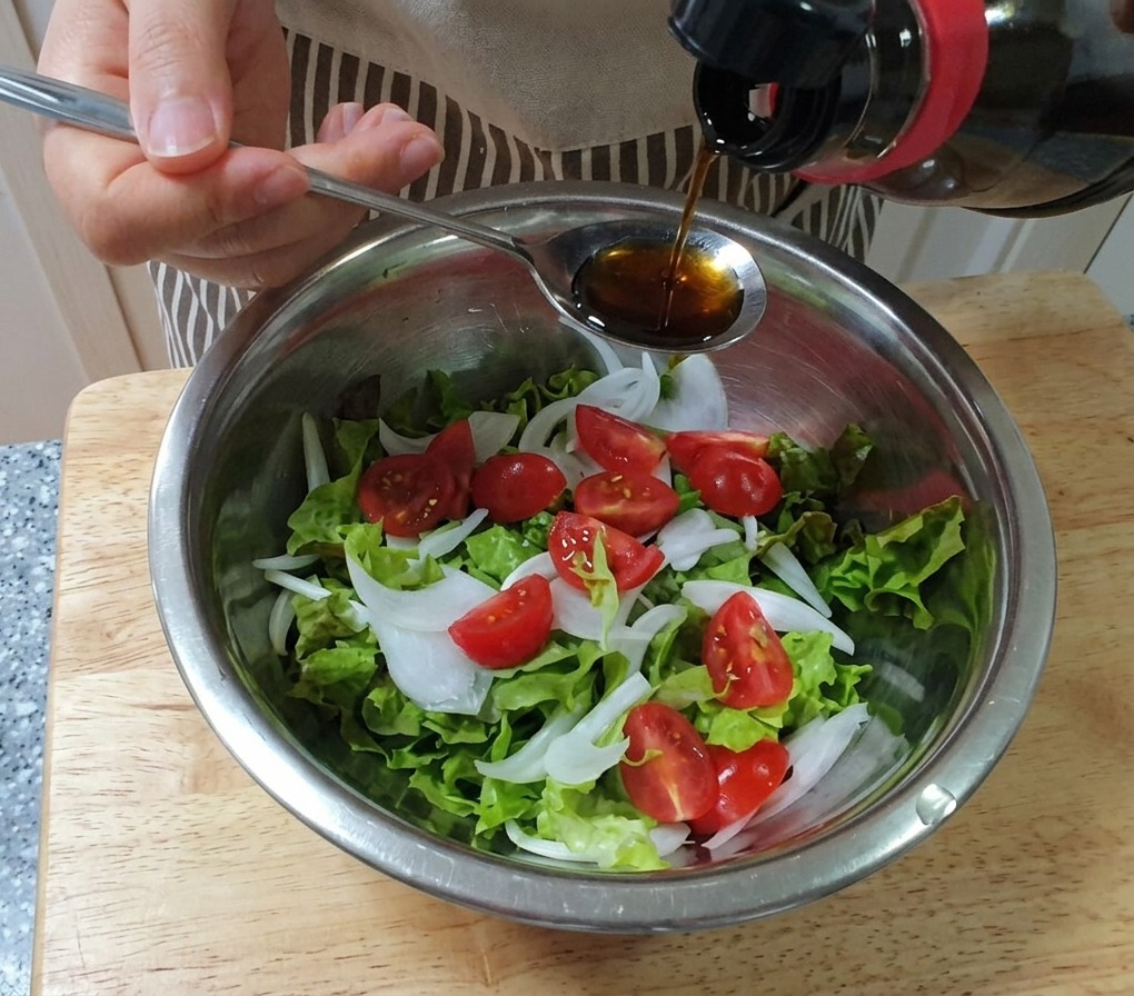 Dressing wird mit einem Löffel über eine Schüssel mit Salat, Zwiebeln und Kirschtomaten gegossen.