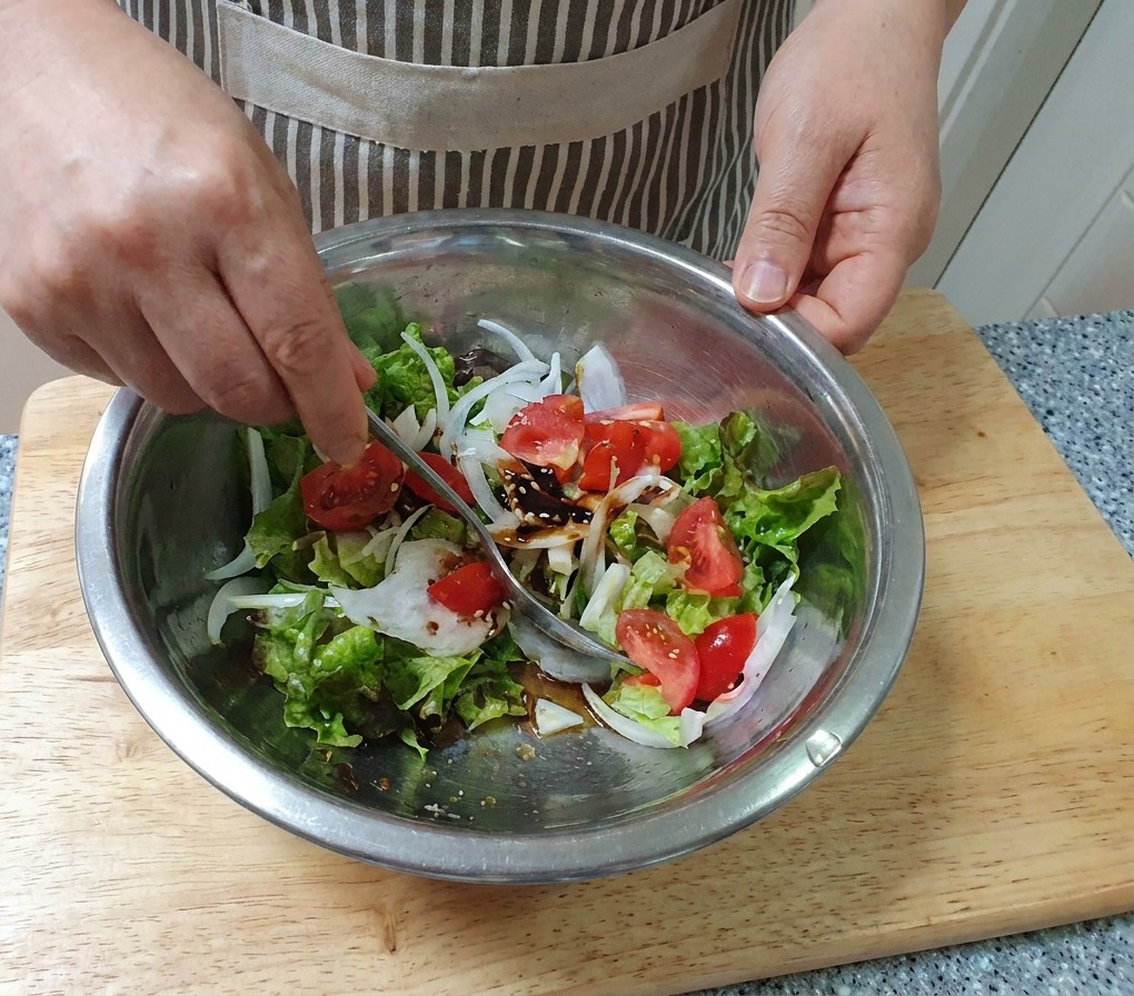 Eine Hand mischt einen frischen Gemüsesalat mit einem Löffel in einer großen Edelstahlschüssel.