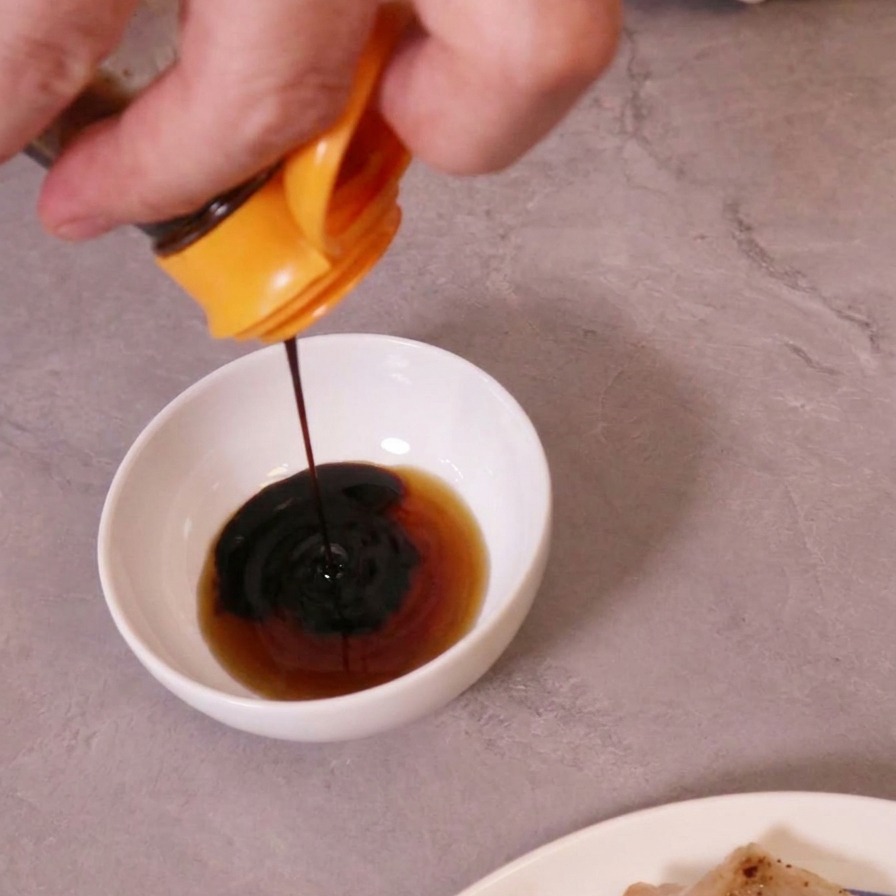 Dunkle Sojasauce wird in eine weiße Schüssel mit einer helleren Flüssigkeit gegossen, um eine Dip-Sauce herzustellen.