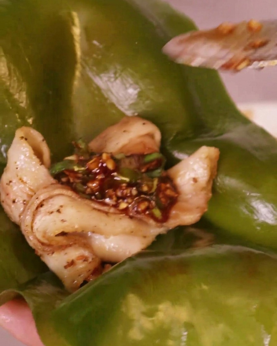 Scharfe rote Chilisauce wird auf ein Stück gegrillten Schweinebauch gegeben, das auf einem grünen Kelp-Blatt liegt.