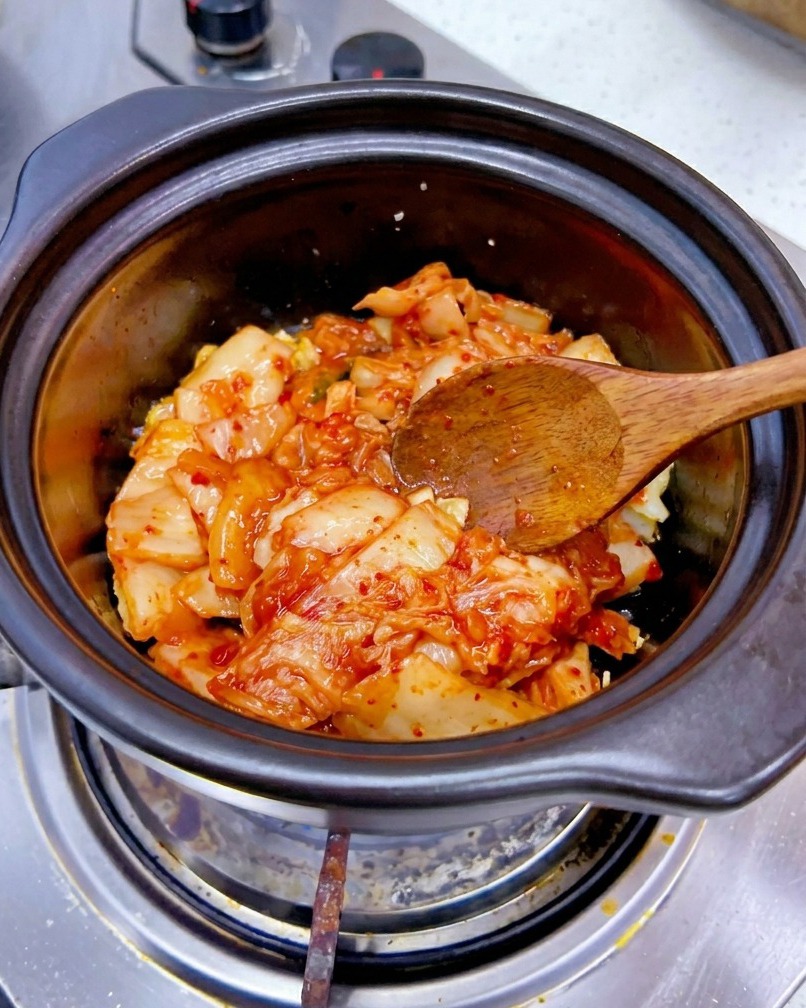 Gehacktes rotes Kimchi wird zu dem angeschwitzten Knoblauch in den Topf gegeben.