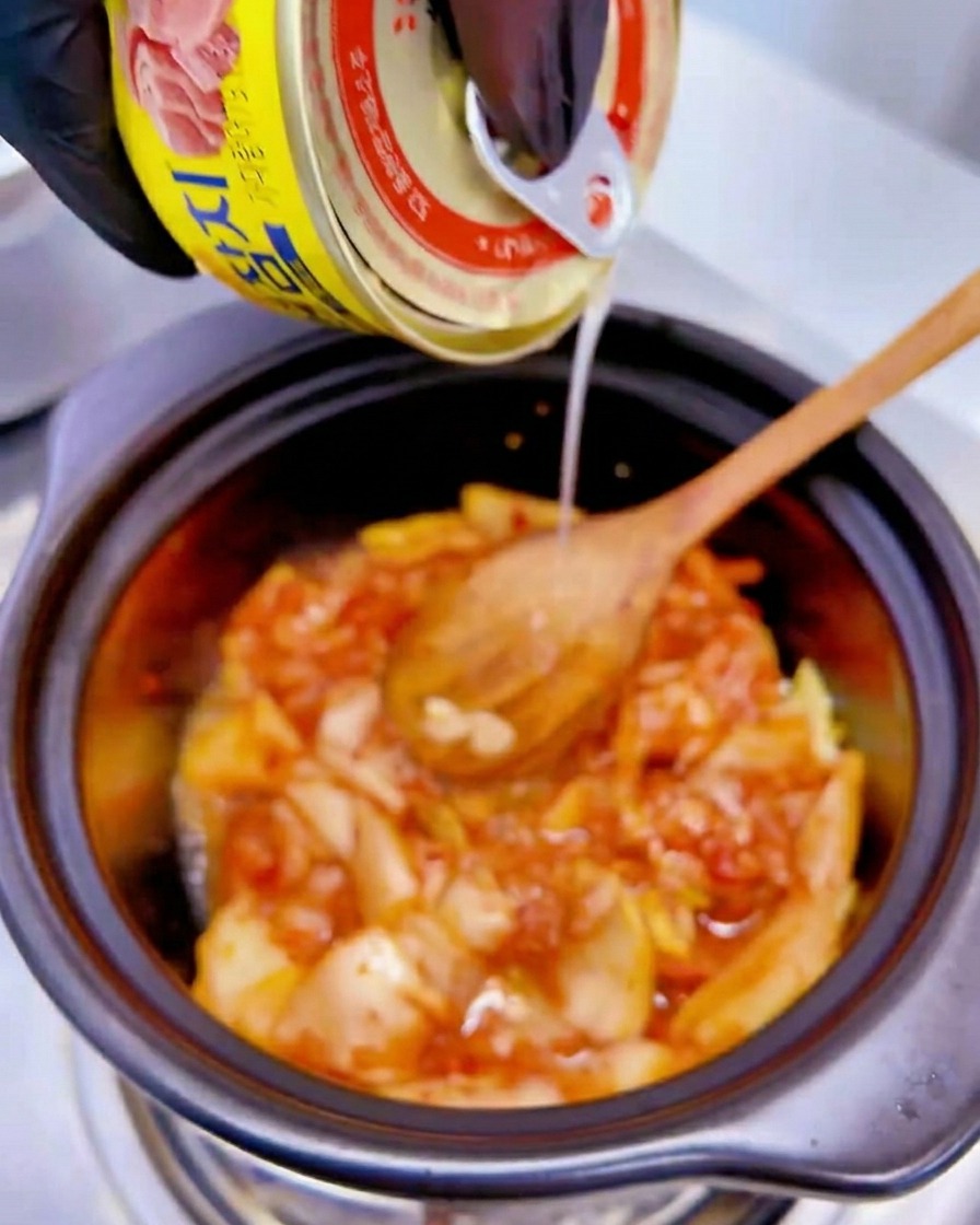 Flüssigkeit aus einer gelben Thunfischdose wird über die Kimchi-Mischung im Topf gegossen.