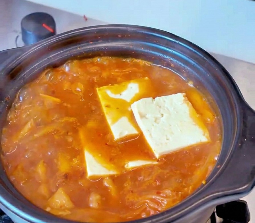 Rechteckige Scheiben von weißem Tofu liegen in einer brodelnden roten Kimchi-Brühe.