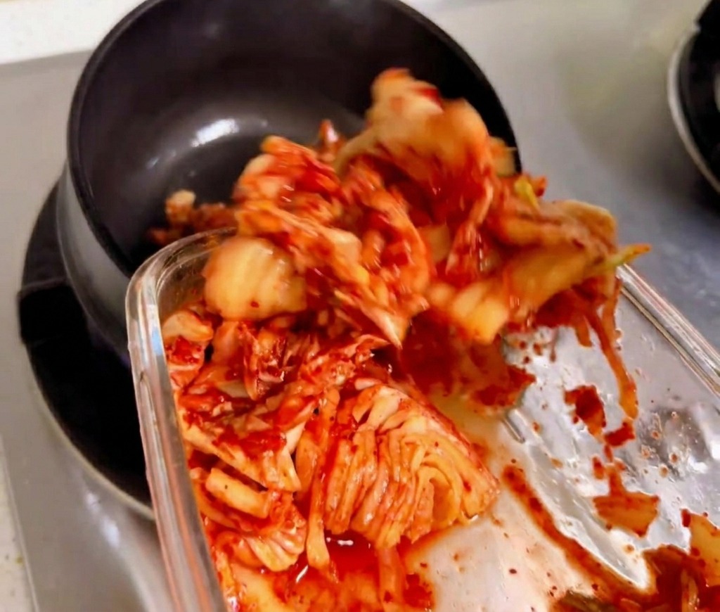 Gehacktes Kimchi wird in einem traditionellen schwarzen Steintopf über einer Gasflamme angebraten.